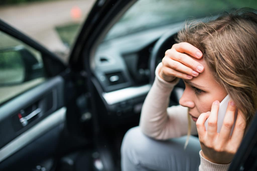 woman with a distressed expression sitting on driver's seat of a car, talking on phone