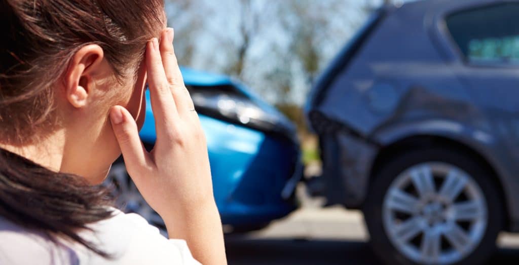 Woman on a roadside holding her head after a car accident