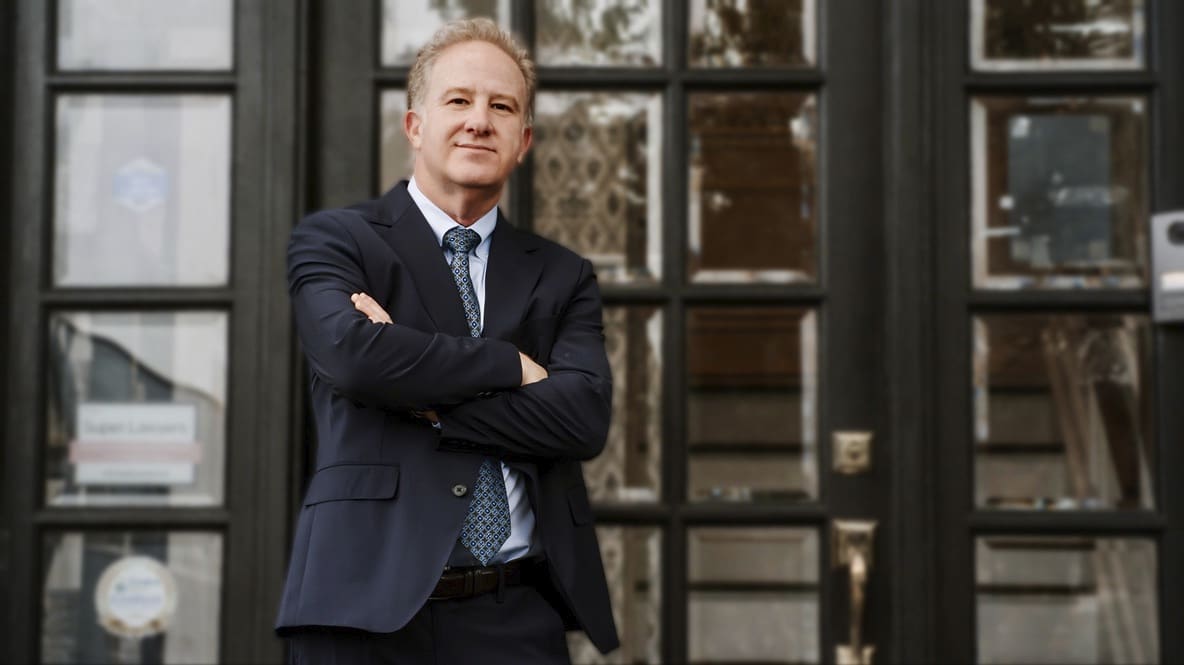 A man in a blue suit jacket standing outside house